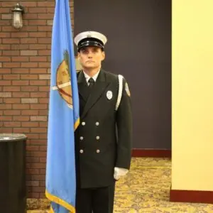Firefighter in uniform standing with flag indoors.