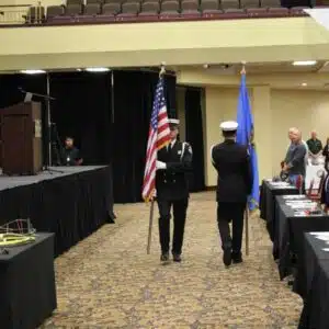 Honor guard carries US and state flags in a ceremony.