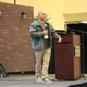Man speaking on stage with a microphone at conference.