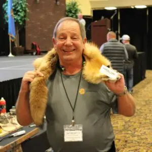 Man holding a fur, smiling at a trade event.