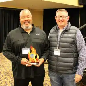 Two men holding an award, smiling at camera.