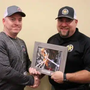 Two men shaking hands while holding a framed photo.