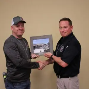 Two men exchanging a framed photo, shaking hands.