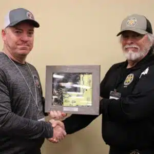 Two men shaking hands while holding a framed picture.
