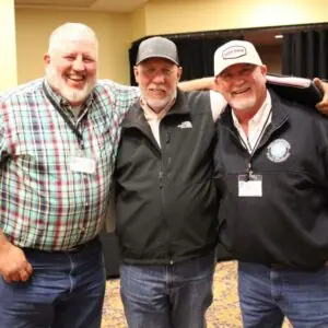 Three men at a conference smiling and hugging.